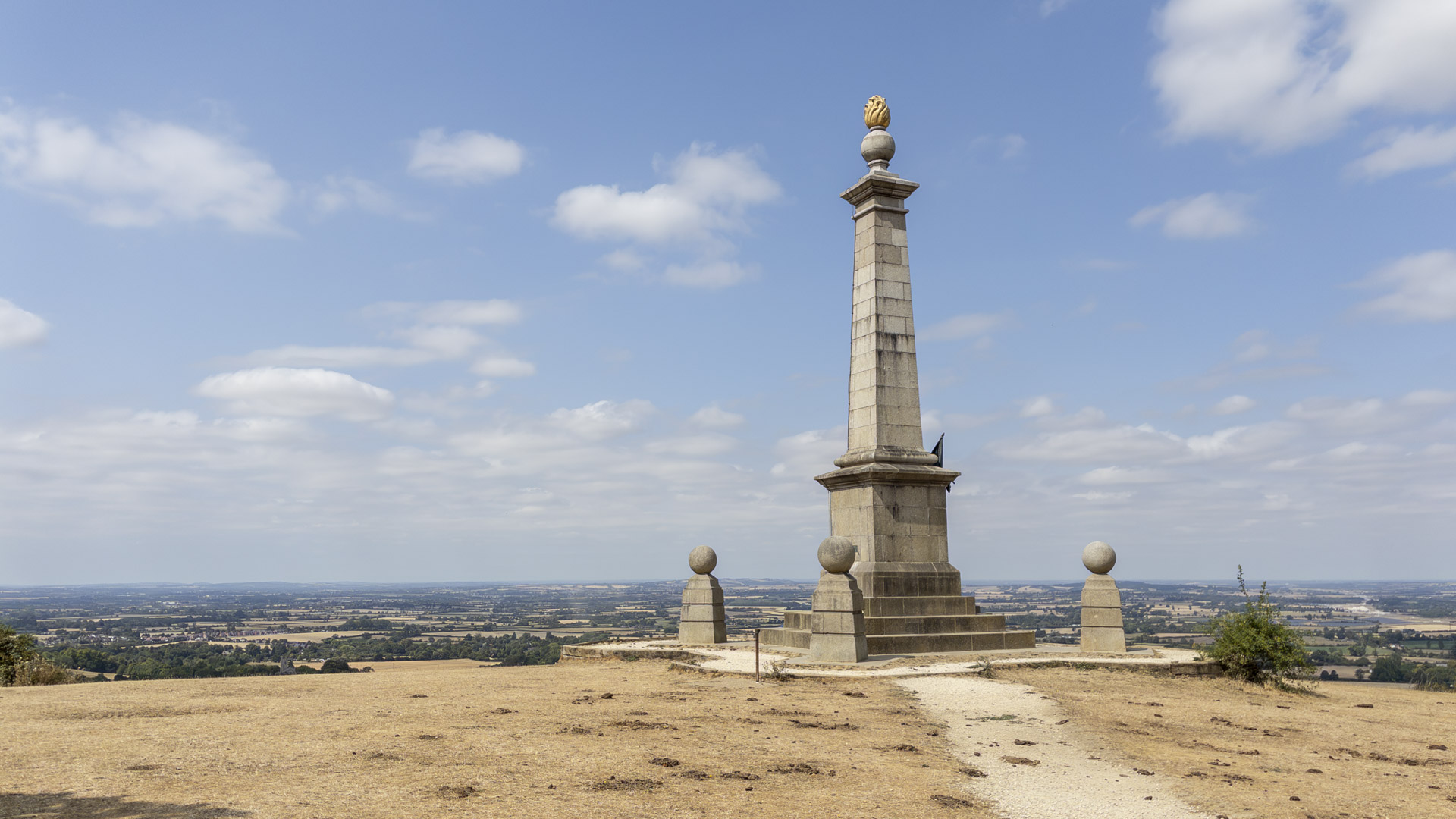 Coombe Hill War Memorial standing on the hilltop, with a tall stone obelisk overlooking wide Chiltern countryside under a blue sky.