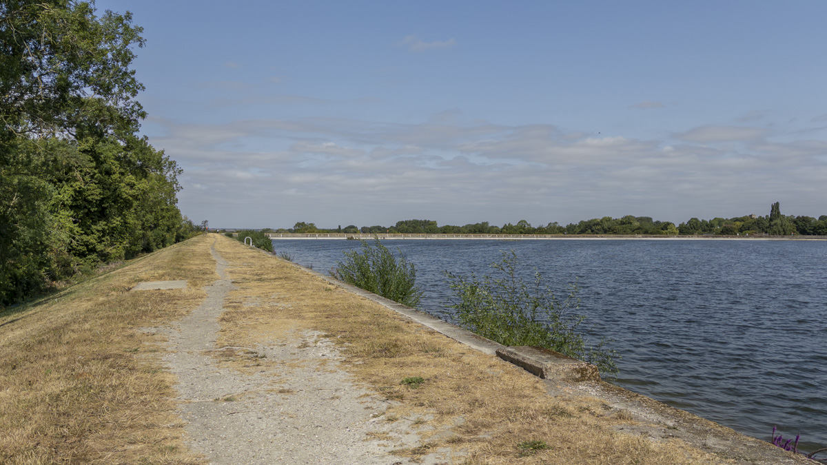 Startop's End Reservoir with a dry path running along the reservoir bank, open water to the right and trees lining the route under a blue sky.