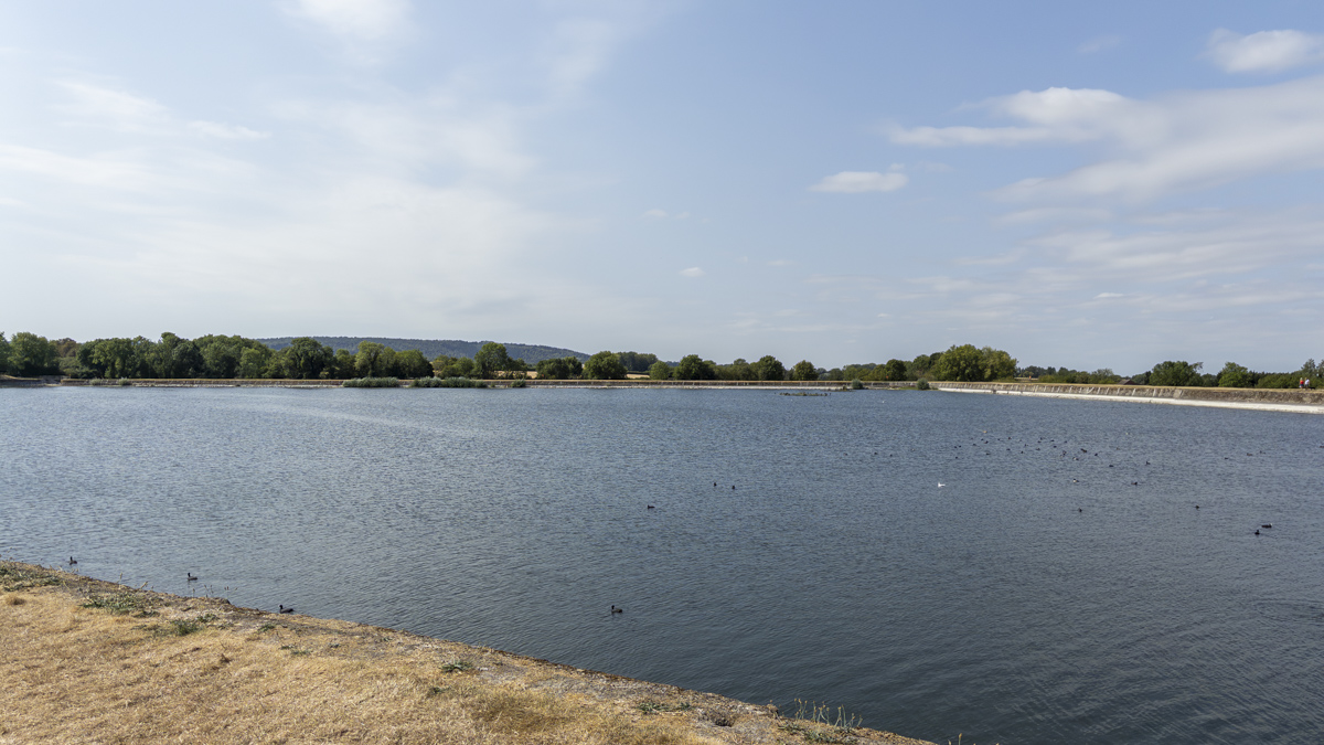 Startops End Reservoir with open water, waterfowl and the reservoir bank curving around the far side beneath a blue, lightly clouded sky.