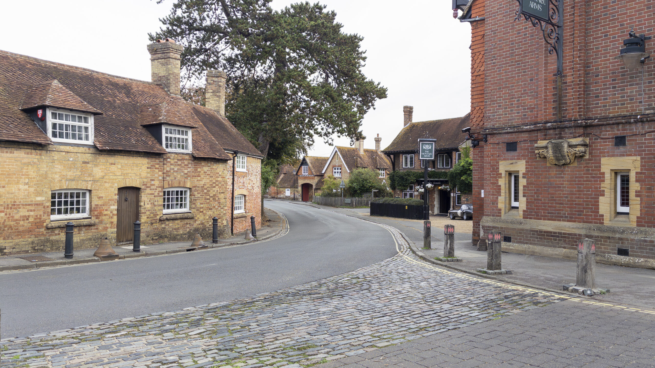 Historic brick cottages and traditional buildings line a curving village street in Beaulieu, New Forest, with cobbled paving in the foreground