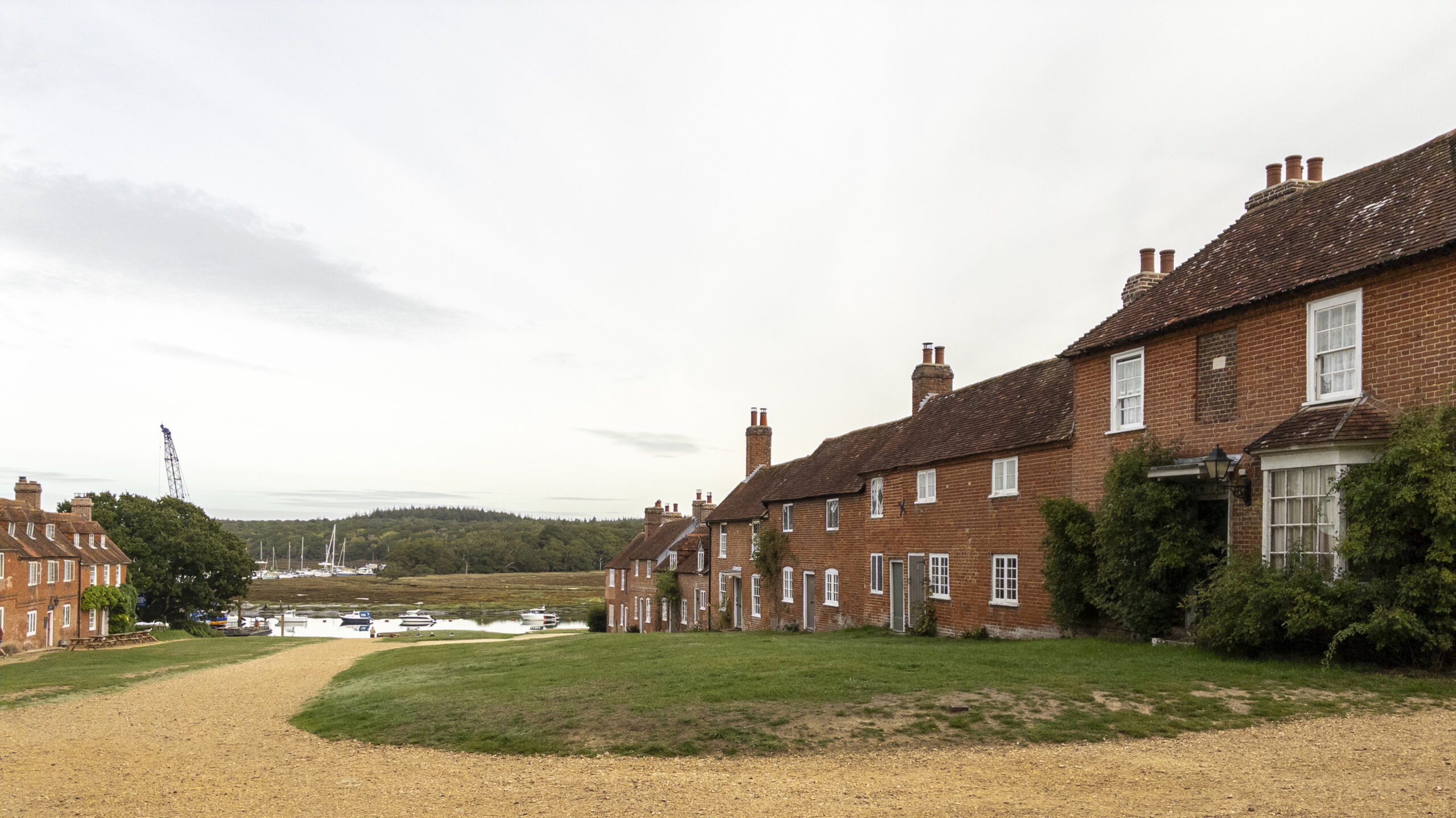 Historic red-brick cottages at Buckler’s Hard overlooking the gravel village path and boats moored on the Beaulieu River estuary